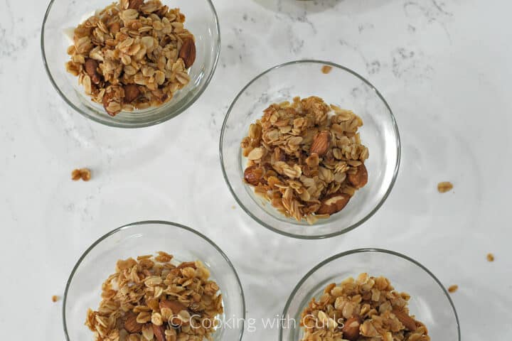 Four small glass bowls with granola topped yogurt.