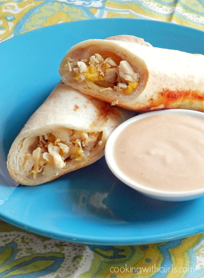 Peachy Chicken Taquitos cut in half and stacked on a plate next to a bowl of creamy adobo sauce.