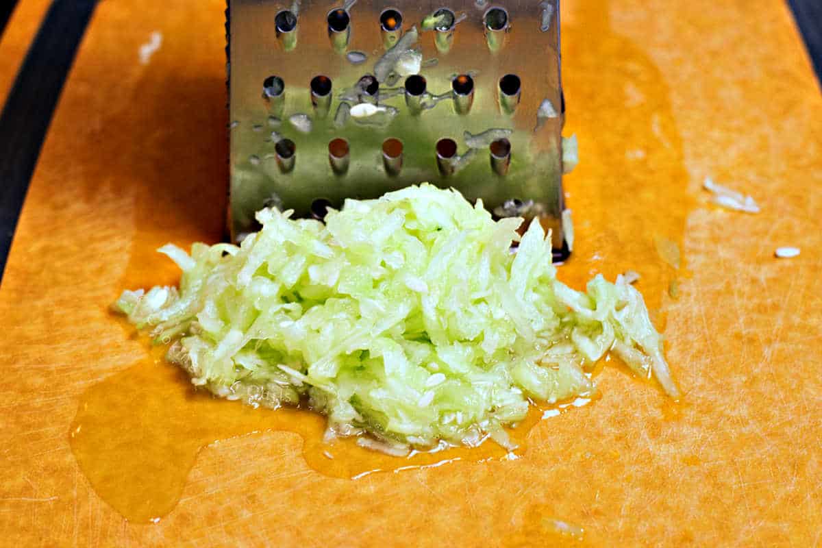Shredded cucumber and grater on a cutting board.