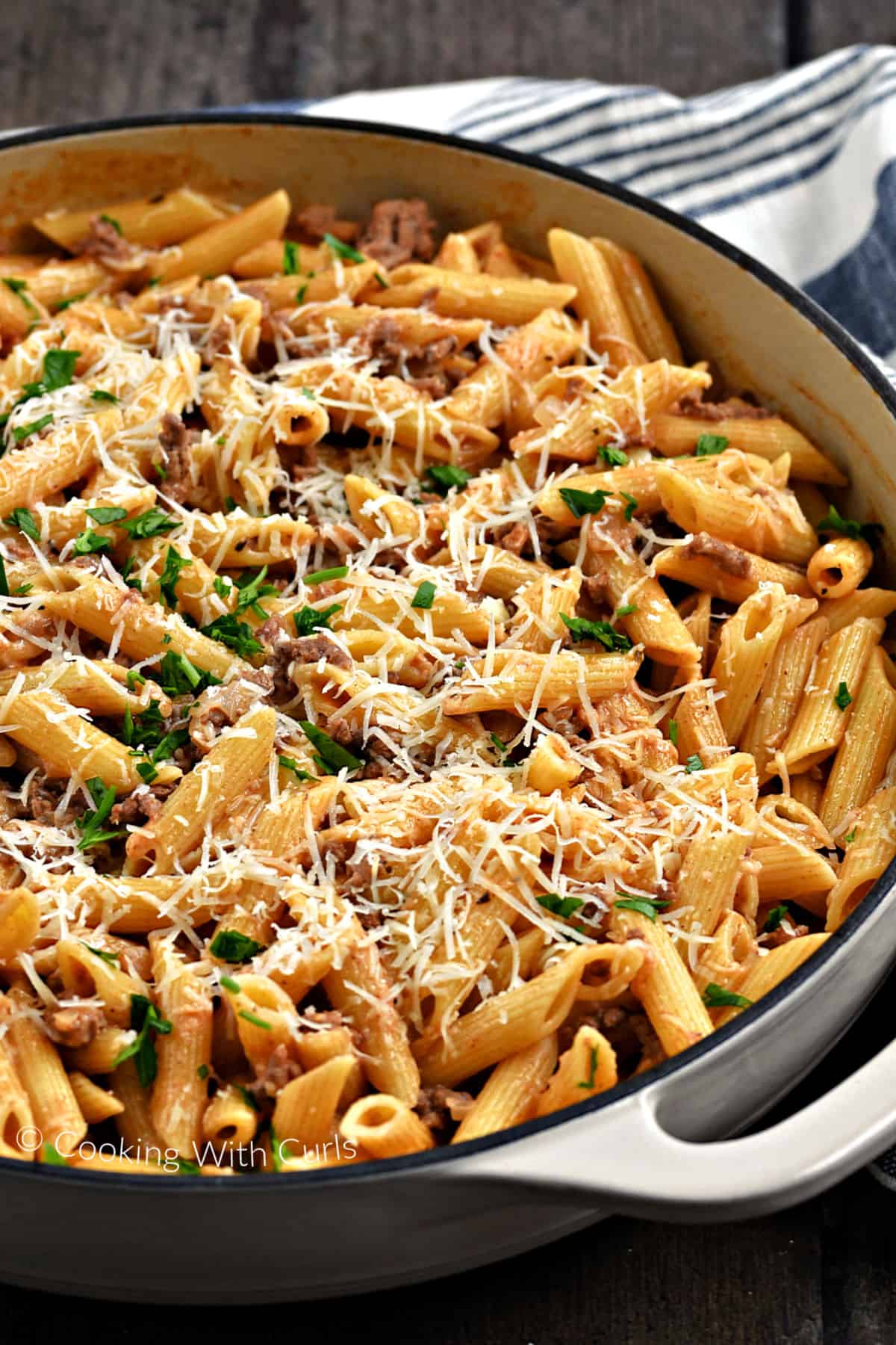 Tubular pasta in a meat sauce topped with grated cheese in a large skillet. 