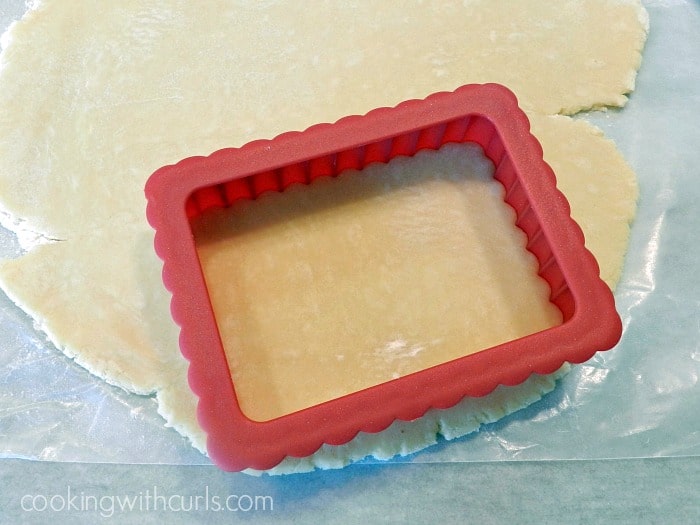 a red, plastic rectangle cutter pushed into rolled out pop tart dough on a marble cutting board. 