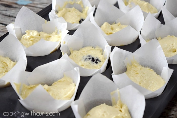 Twelve white paper liners filled with muffin batter in a muffin tin.