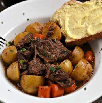 Chunks of beef roast, potatoes, and carrot slices in a Guinness stout gravy with buttered bread on the edge of the bowl.