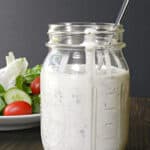 homemade dairy free ranch dressing in a glass mason jar with a spoon sticking out the top, sitting in front of a green salad.