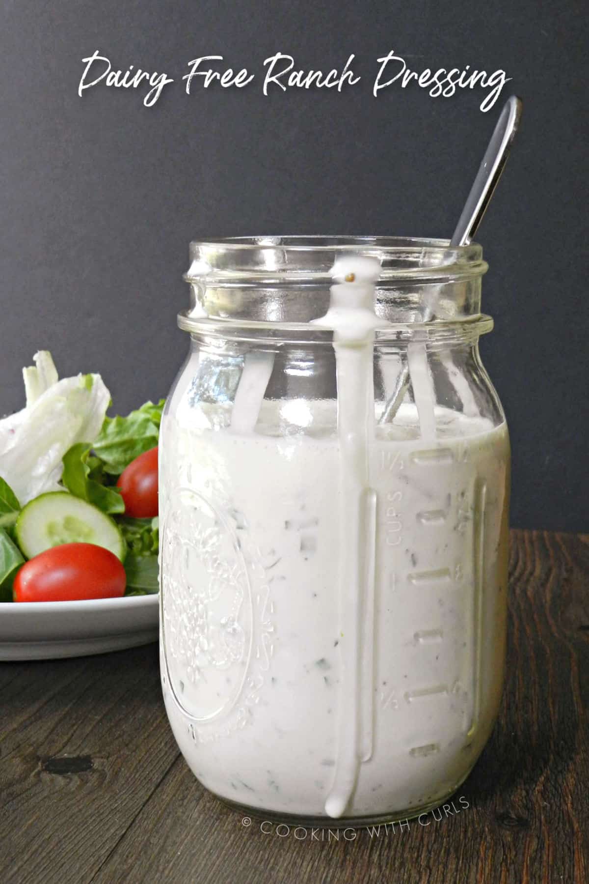 homemade dairy free ranch dressing in a glass mason jar with a spoon sticking out the top, sitting in front of a green salad.