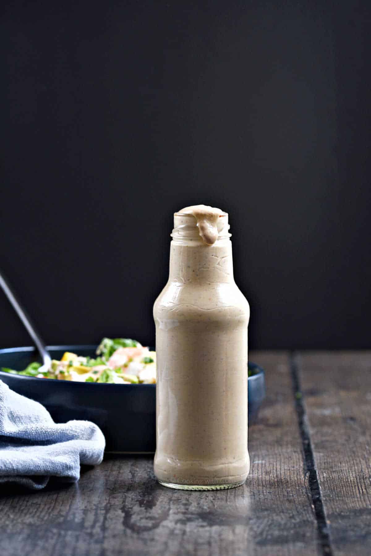 A bottle of thousand island dressing with a bowl of salad in the background.