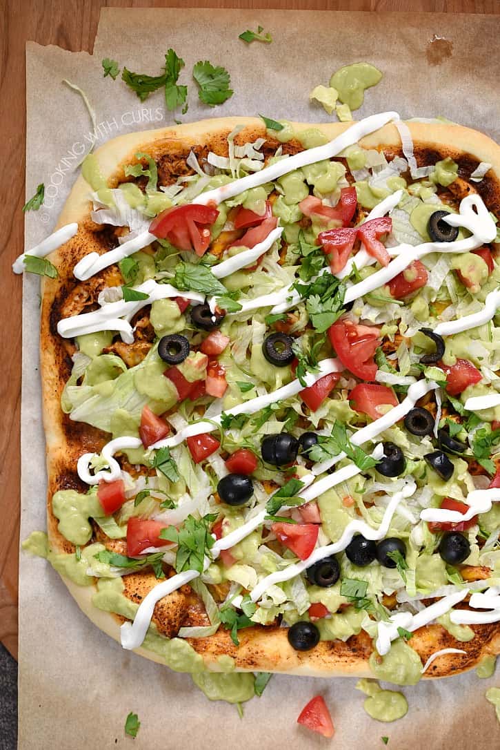 A rectangle pizza topped with lettuce, chicken, tomatoes, olives, guacamole, and sour cream.