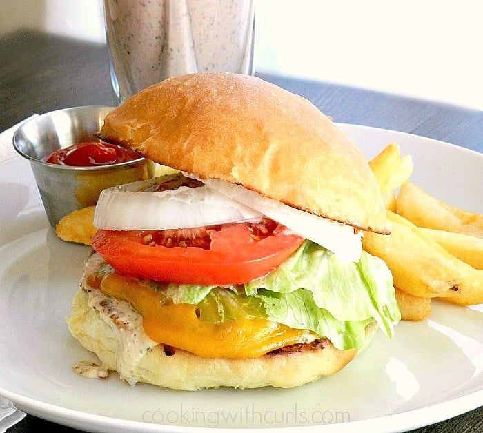 A burger covered in melted cheese, thousand island dressing, lettuce, onion, and tomato with a side of fries.