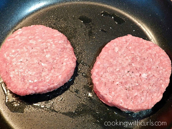 Two raw ground beef patties in a skillet.