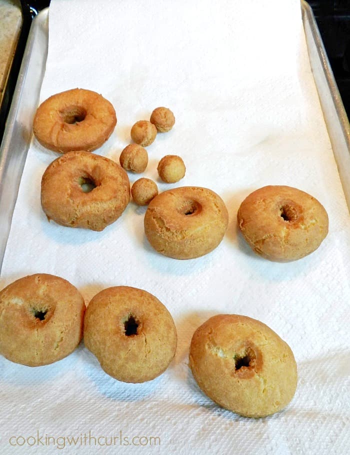 Seven fried doughnuts and five doughnut holes sitting on paper towels on a baking sheet.