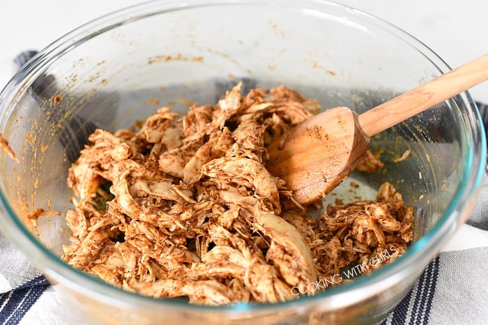Shredded chicken mixed with enchilada sauce in a bowl.