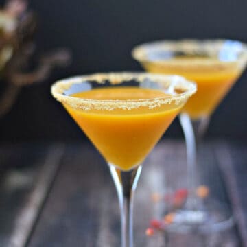 Two pumpkintini filled martini glasses with graham cracker crumbs around the rims.