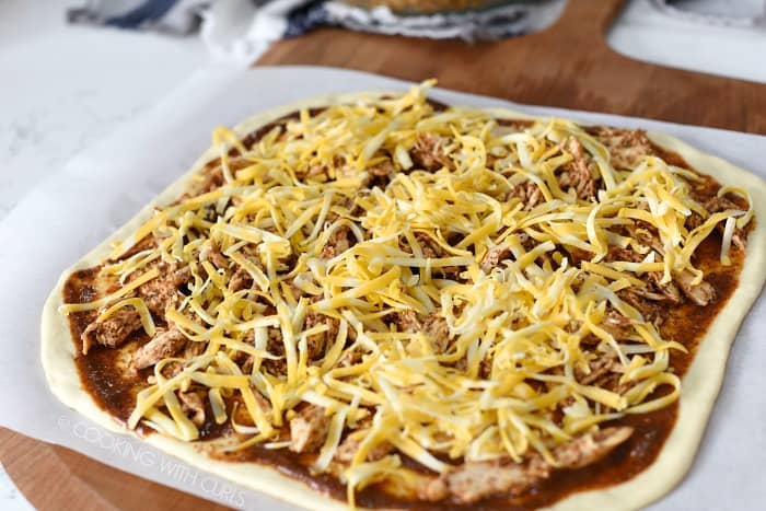 Raw pizza dough topped with enchilada sauce, chicken, and shredded cheese.