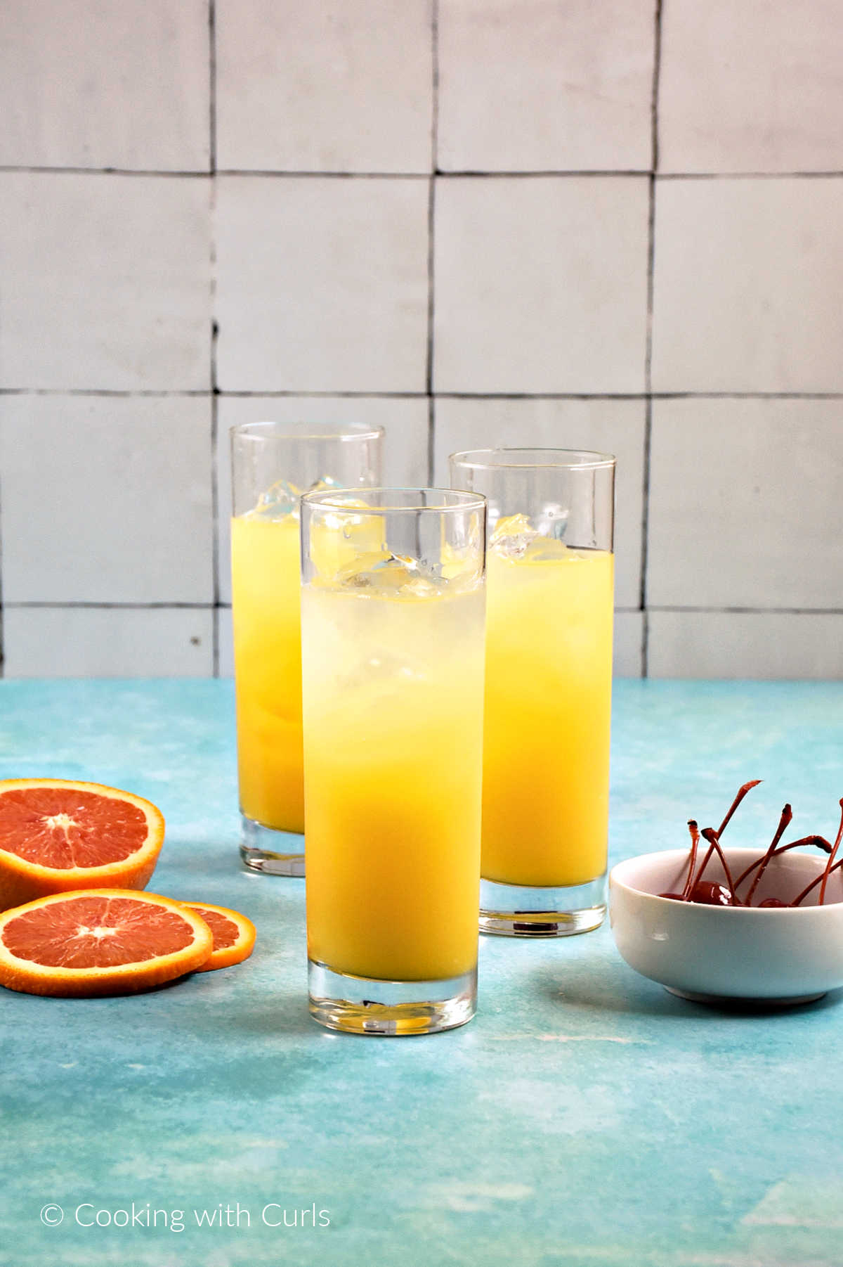 Three tall glasses with ice cubes, orange juice and tequila.