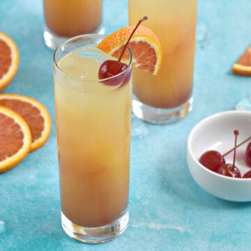 Three ice filled highball glasses filled with tequila sunrise cocktails with orange and cherry garnish.
