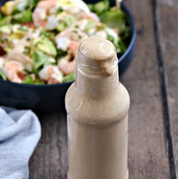 A jar of thousand island dressing with bowl of salad in the background.