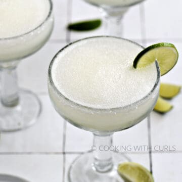 A frozen blended margarita garnished with a lime wheel in a thick margarita glass.