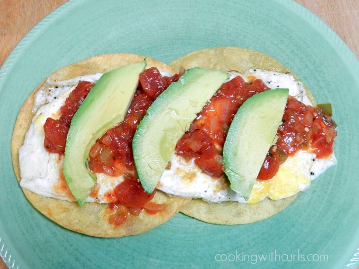 Traditional Huevos Rancheros with chunky sauce and avocado slices on a green plate