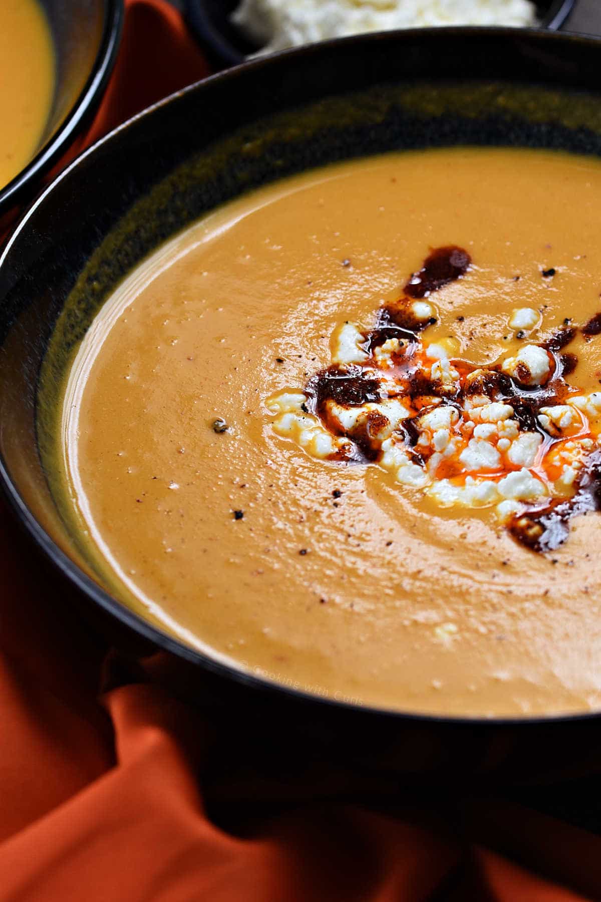 A bowl of creamy orange soup with feta and harissa.