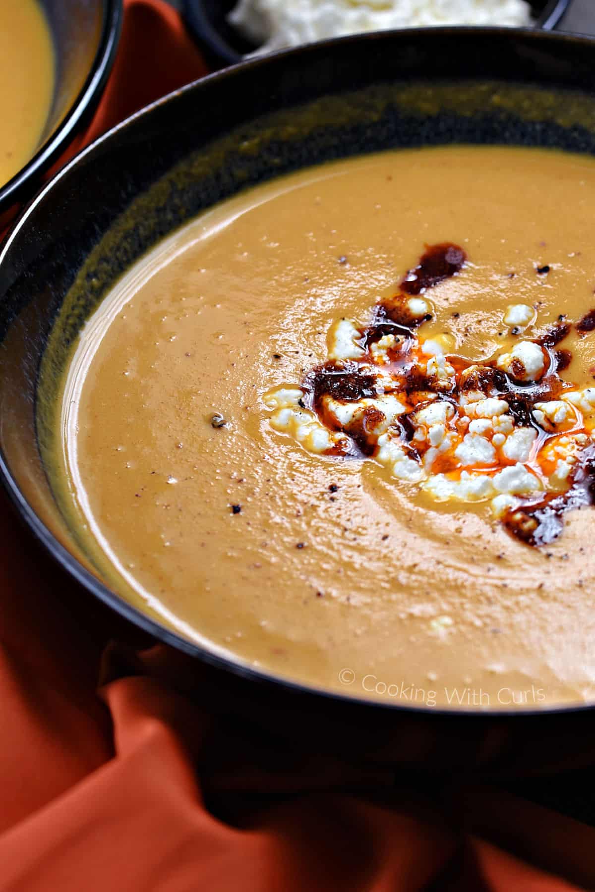 A close-up image of butternut squash soup in a bowl with feta crumbles and chili sauce down the center. 