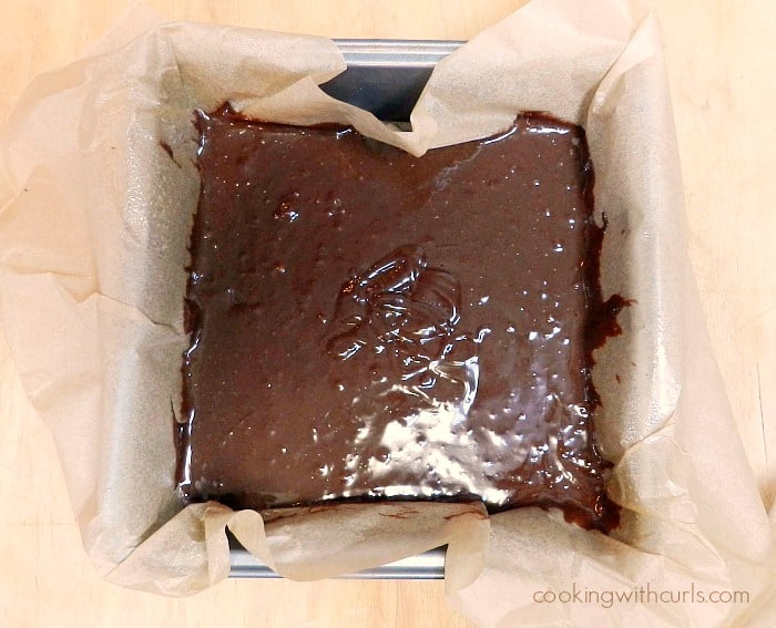 Brownie batter in a parchment lined baking pan cookingwithcurls.com
