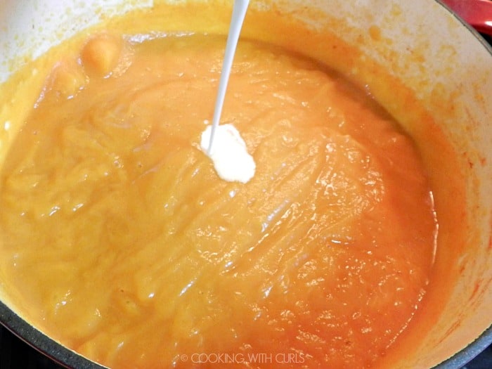 Cream being added to the squash soup in the pot. 