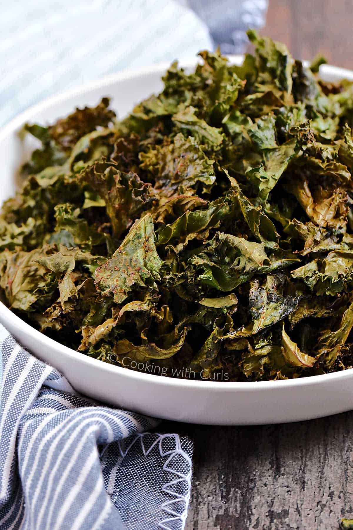 A bowl filled with seasoned kale chips sitting on a blue and white striped napkin.