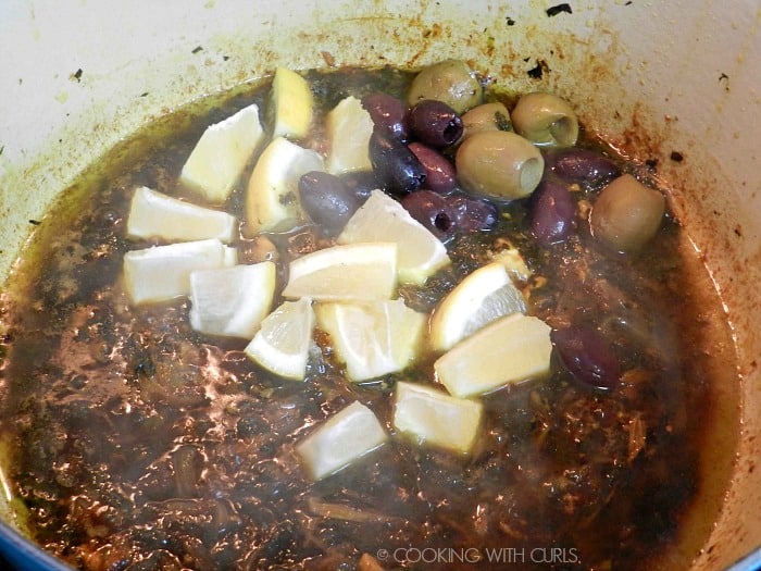 Lemon wedges and olives added to the sauce in the Dutch oven