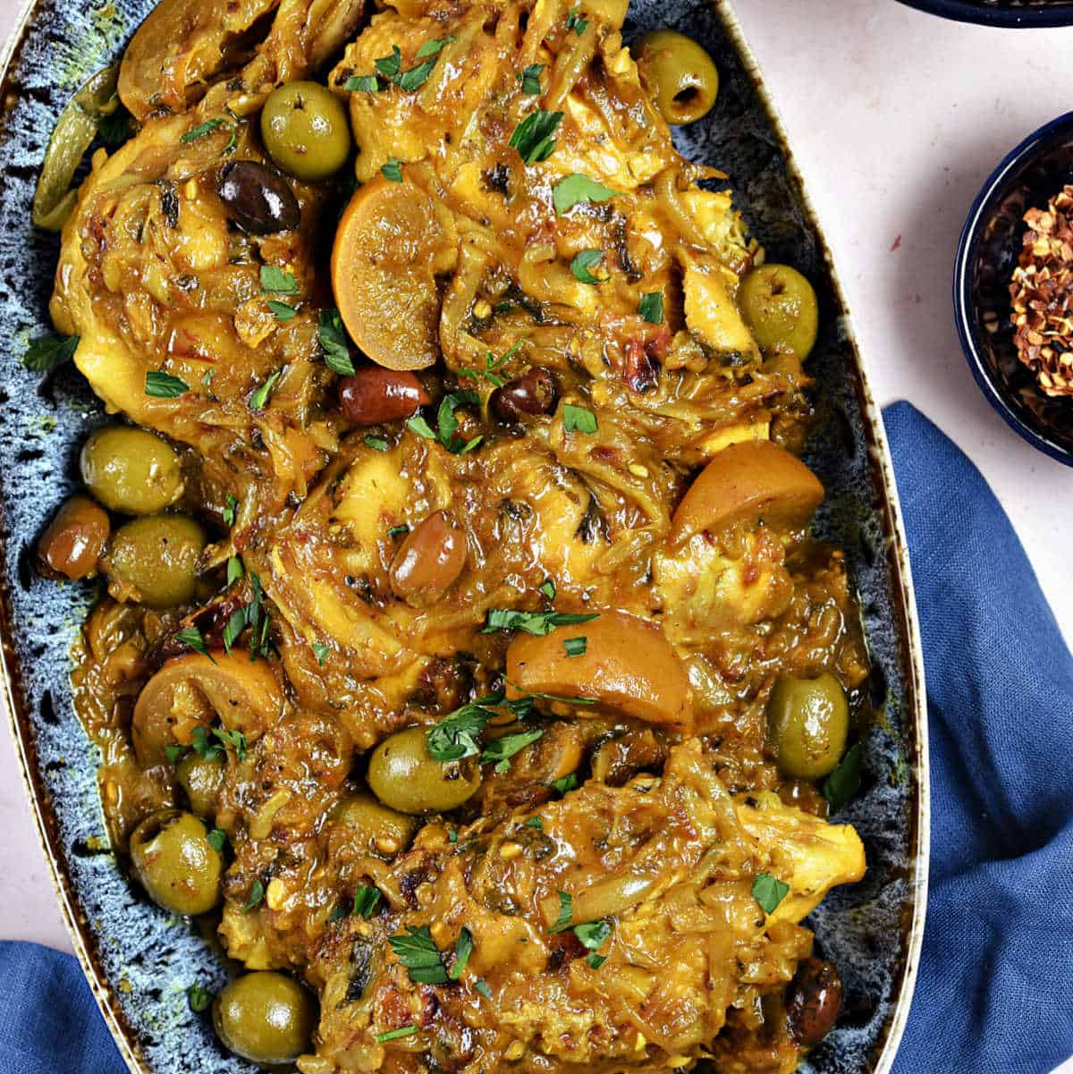 Moroccan spiced chicken pieces, sliced onions, olives, and lemon wedges in a serving dish.