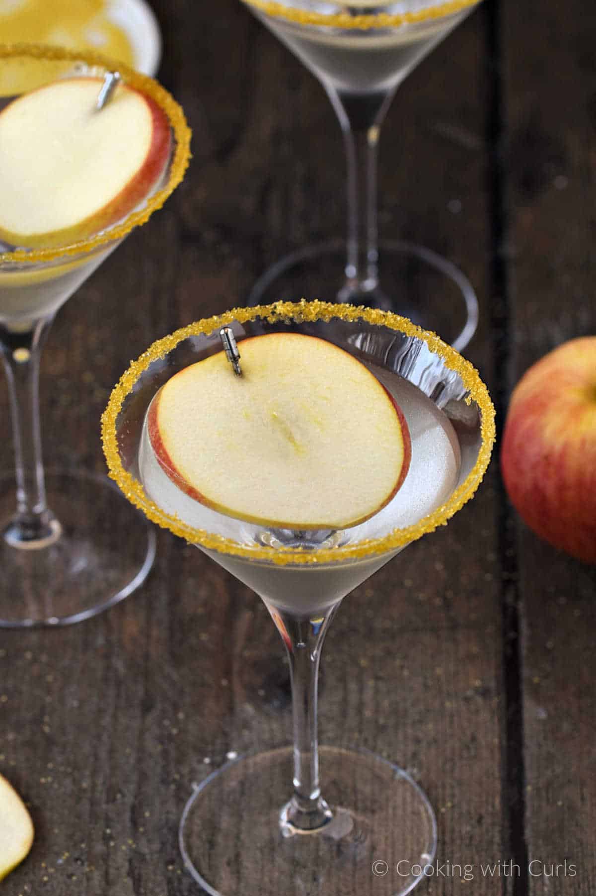 A sugar rimmed martini glass with caramel and apple vodka and an apple slice floating on top.