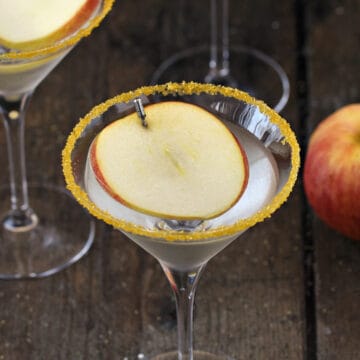 A sugar rimmed martini glass with caramel and apple vodka and an apple slice floating on top.