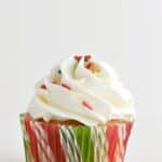 white frosting topped cupcake with red and green wrapper and sprinkles
