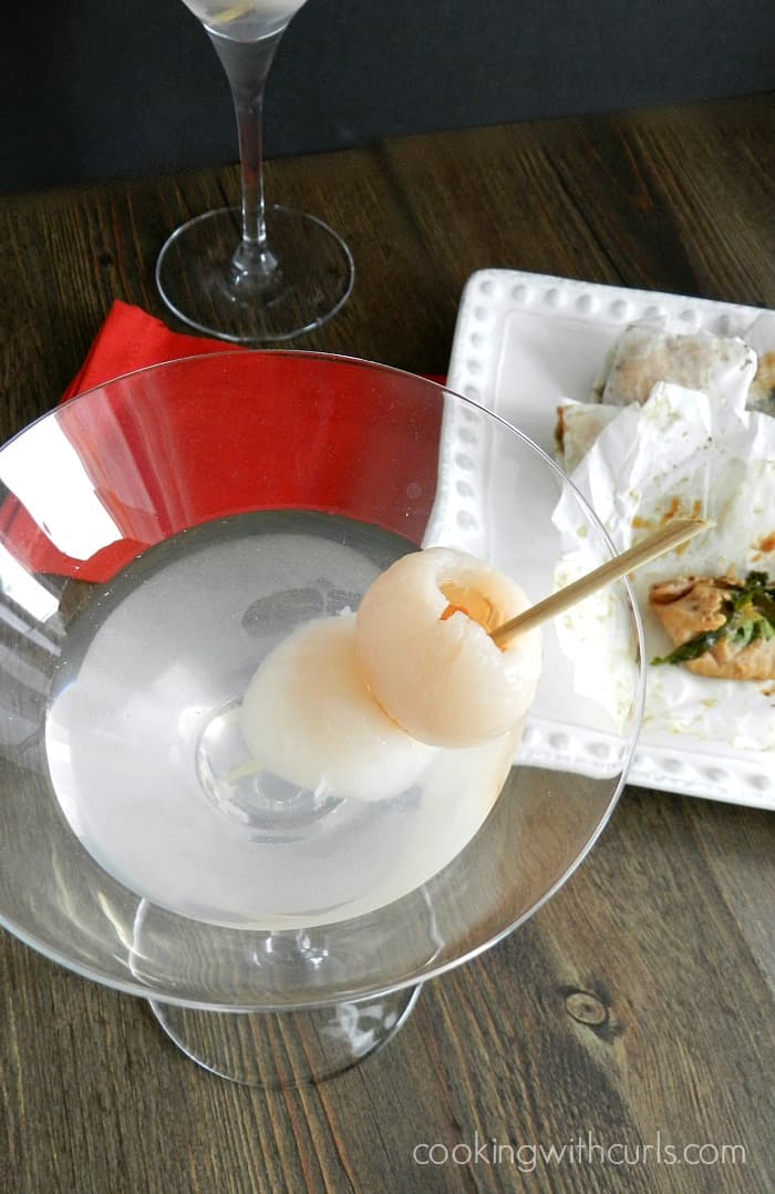 lychee martini with two lycheese on a tooth pick with paper wrapped chicken off to the right