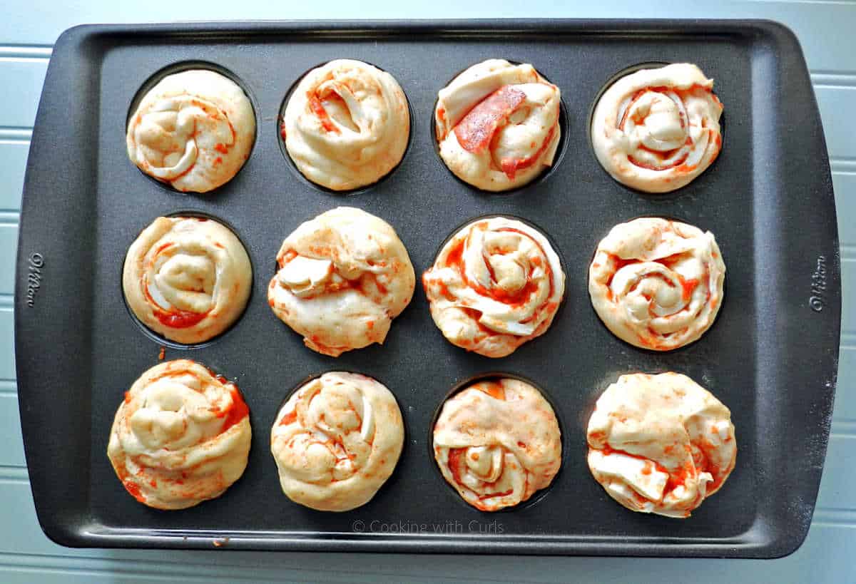 Pepperoni pizza rolls rising  in a muffin tin.