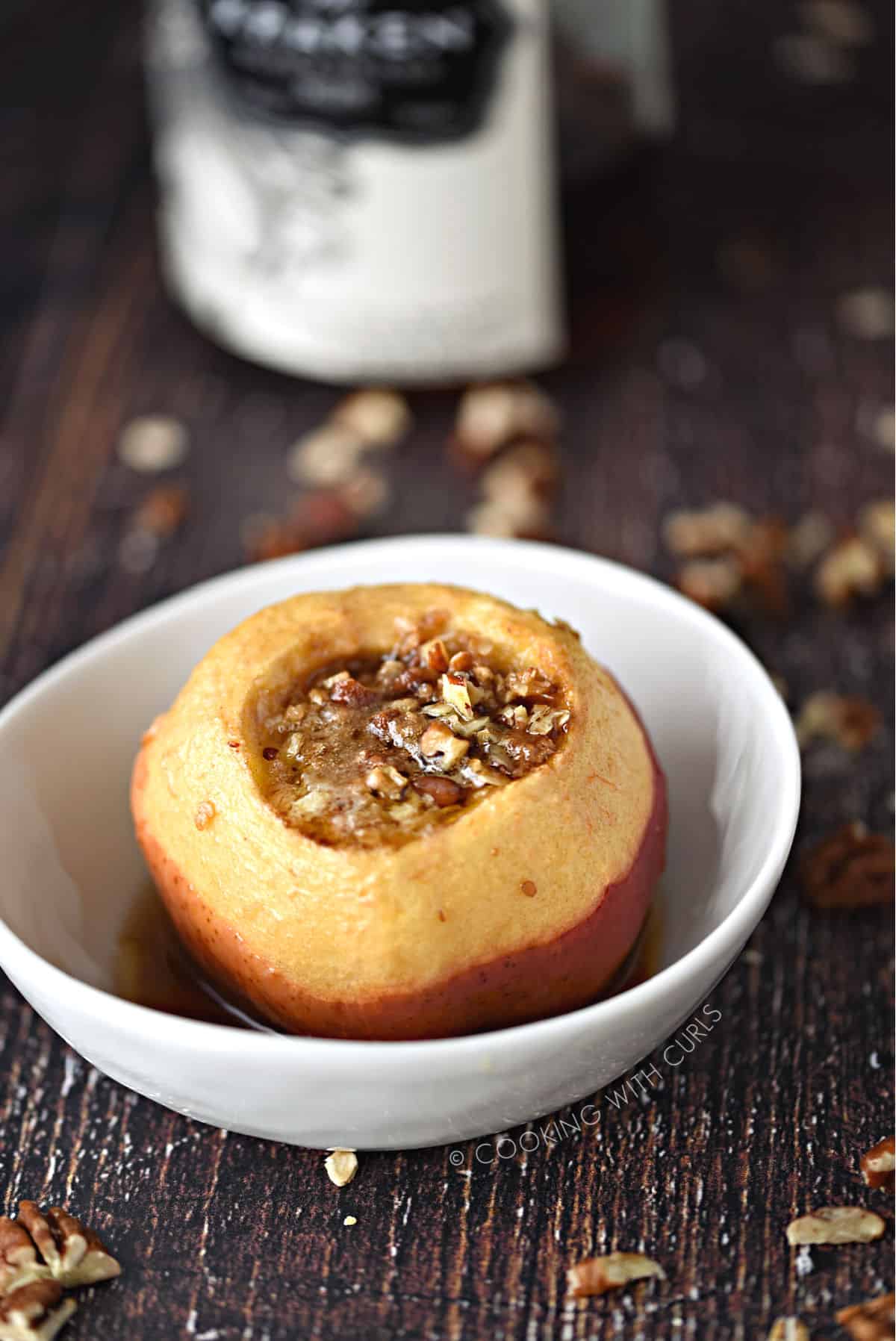 Spiced Rum Baked Apples filled with oats, pecans, brown sugar and butter in a small white bowl with a bottle of spiced rum in the background.