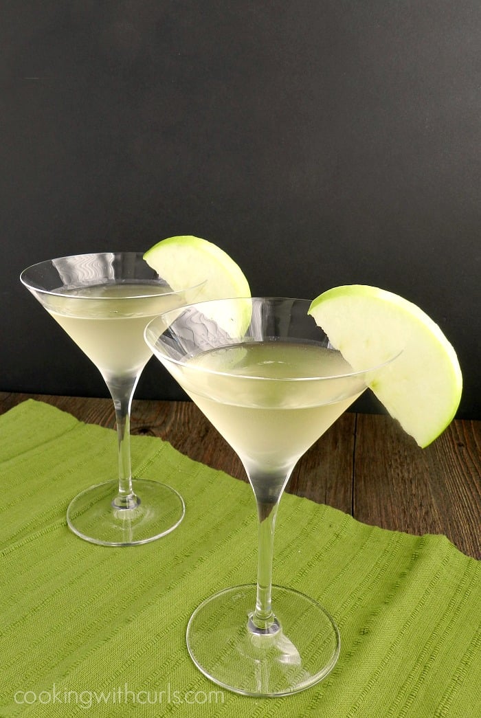 Two martini glasses on a green napkin filled with caramel apple martinis and garnished with green apple slices.