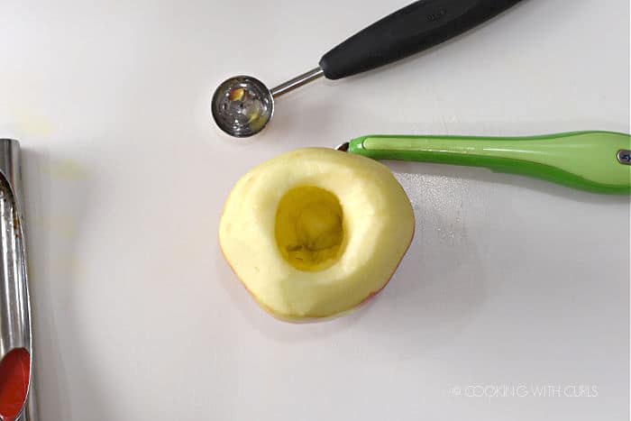 looking down on an apple that has been cored with a melon baller and apple corer, and partially peeled with a vegetable peeler. 