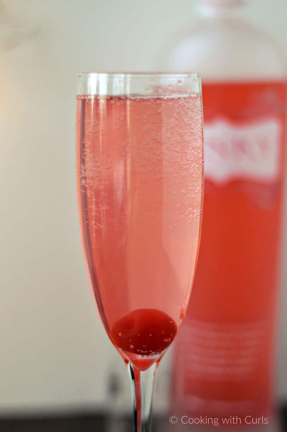 A champagne flute filled a bubbly, pink cocktail and a cherry at the bottom. 
