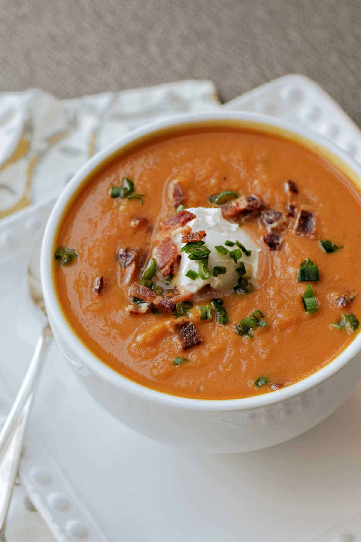 A bowl of creamy pumpkin soup topped with yogurt, bacon bits, and green onions.