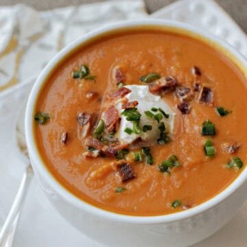 A bowl of creamy pumpkin soup topped with yogurt, bacon bits, and green onions.