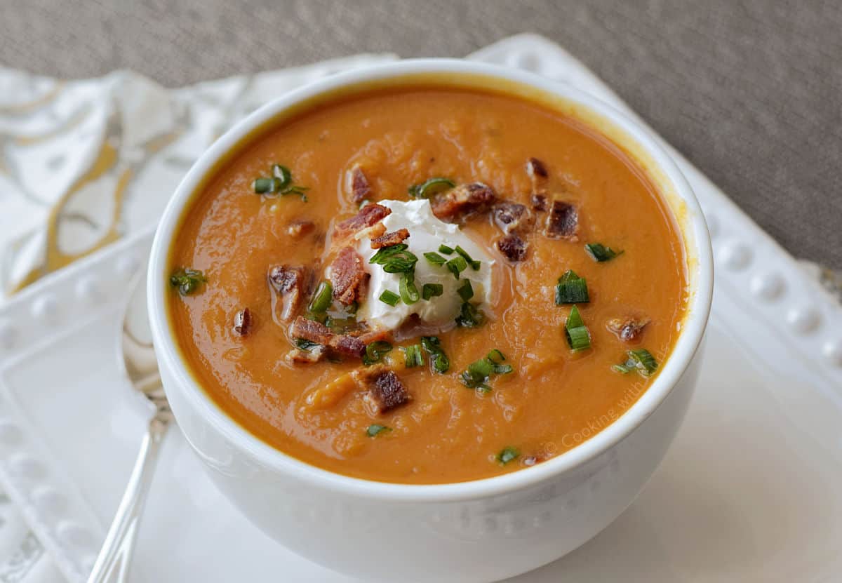 A bowl of creamy pumpkin soup topped with yogurt, bacon bits, toasted pumpkin seeds, and green onions.