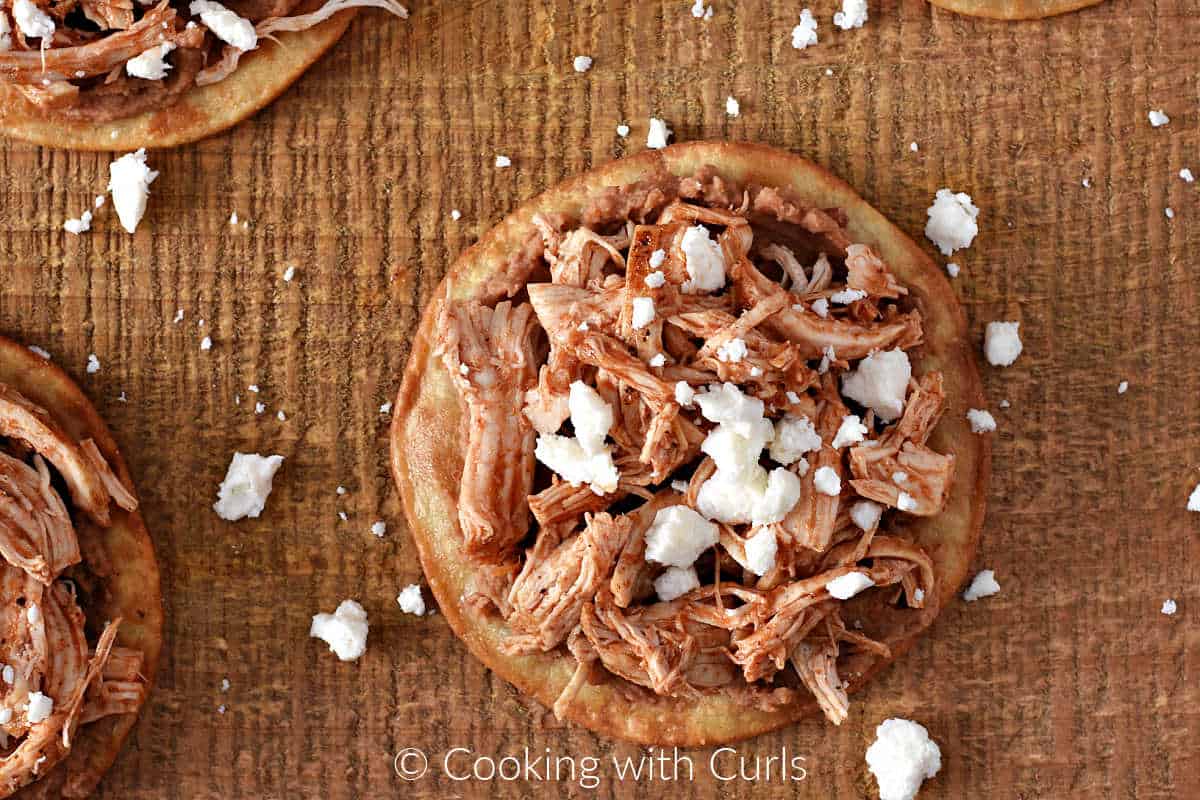 Crispy tostada shell topped with refried beans, shredded chicken, and crumbled queso.