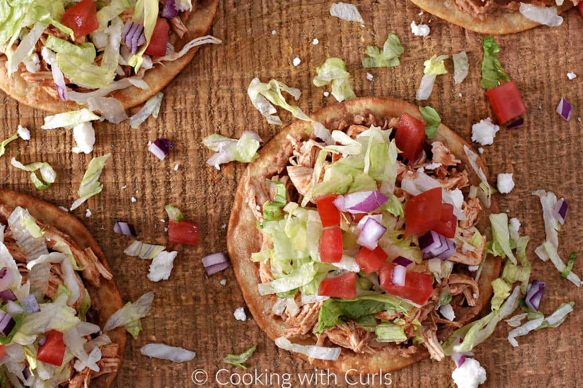 Tostada shells topped with chicken, beans, lettuce, tomato, cheese, onion, and cilantro.