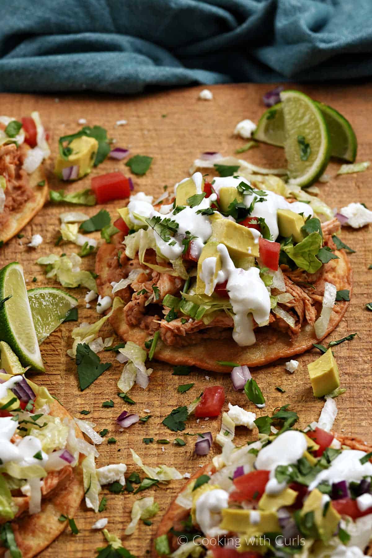 Four chicken tostadas on a wood serving board with lime wedges.