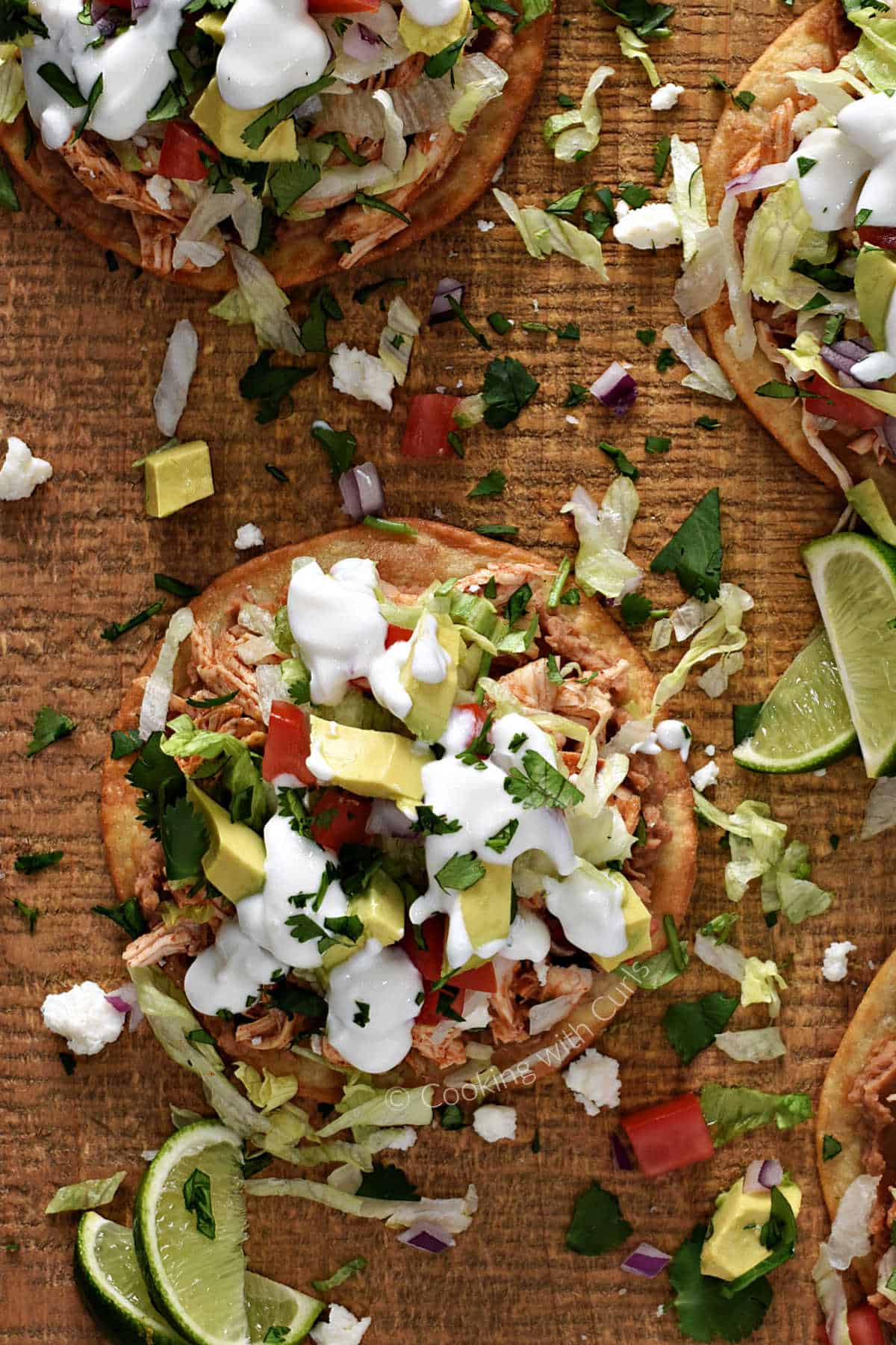 Looking down on three chicken tostadas with traditional toppings on a wood serving board.