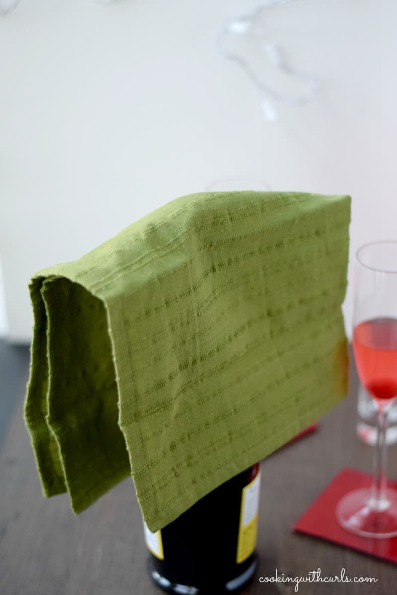 A bottle of Prosecco with a green towel draped over the top.