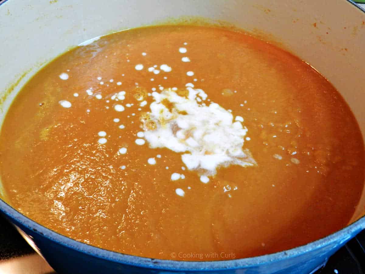 Pureed pumpkin soup in dutch oven with cream poured in the center.