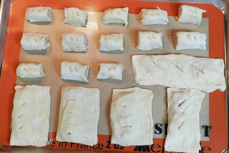 A silicone lined baking sheet with multiple sizes of sausage rolls.