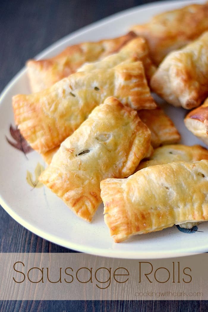 sausage rolls wrapped in puff pastry piled up on a beige plate with a falling leaves motif