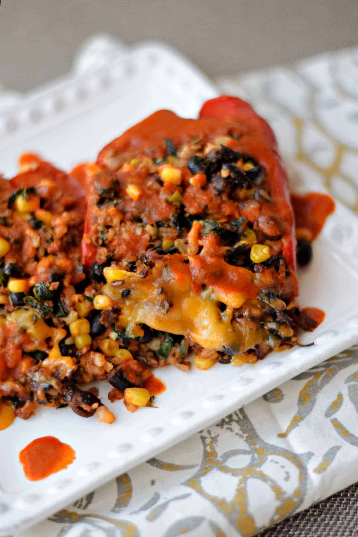 Two stuffed peppers with melted cheese and enchilada sauce on a plate.